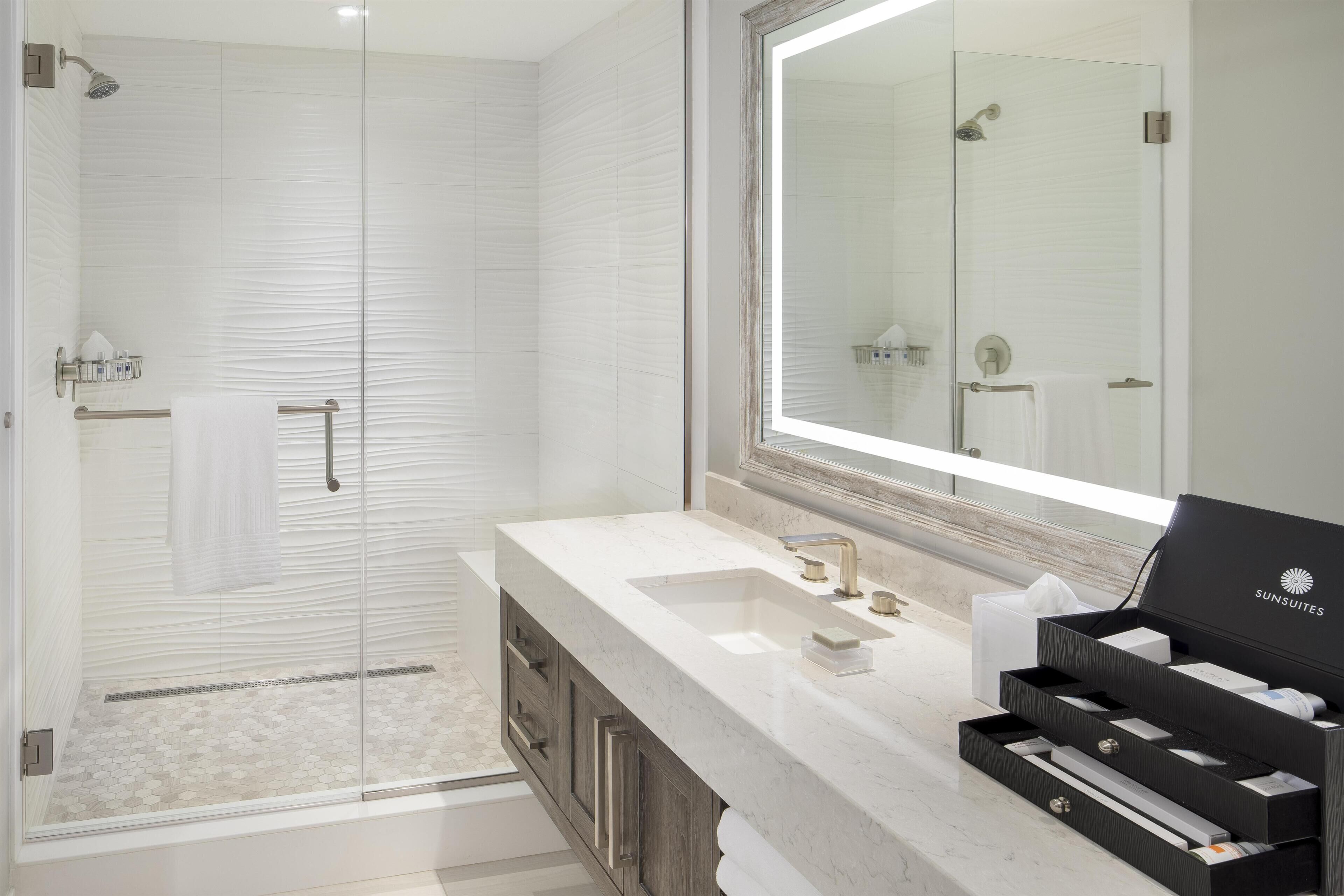 Une salle de bain moderne dotée d’une douche à parois de verre, d’un grand miroir et d’un meuble-lavabo avec un évier et un porte-serviettes.