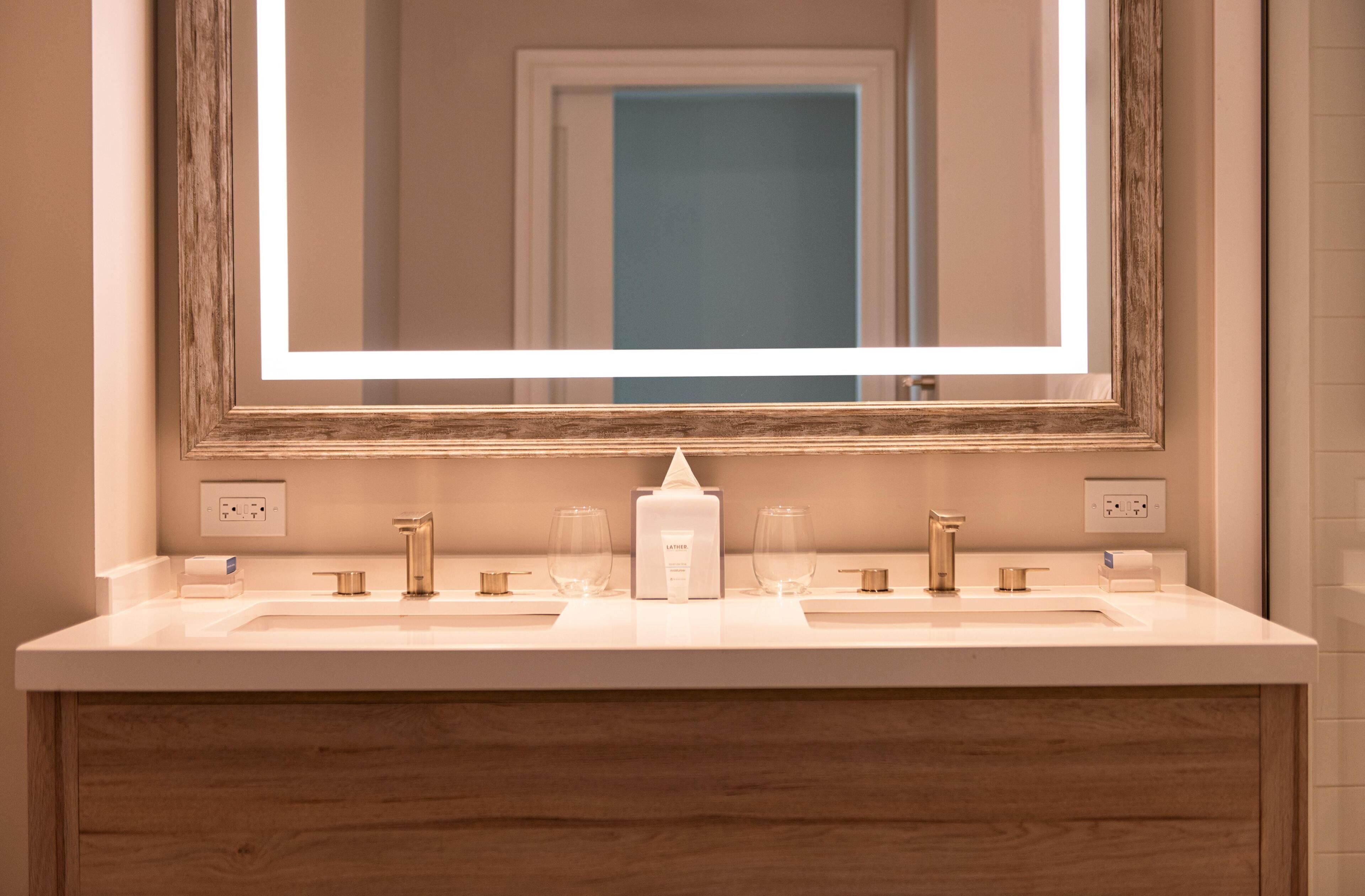 A bathroom with a white vanity, a mirror with a wooden frame, and a lighted mirror.