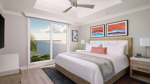 A hotel room with a large bed, a ceiling fan, a view of the ocean, and artwork on the wall. - Sunsuites Villas At Sunseeker Resort, Curio By Hilton (Charlotte Harbor)