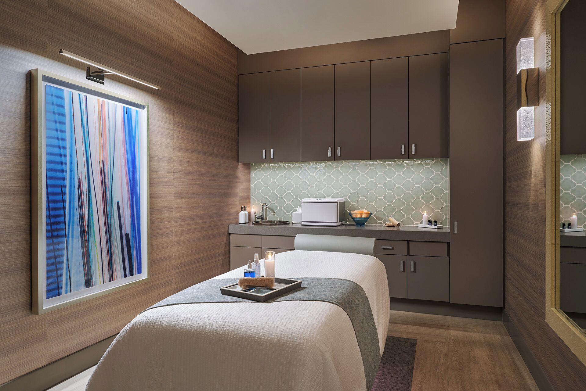 A modern hotel room with a large abstract painting, a kitchenette with a microwave, and a small seating area with a tray.