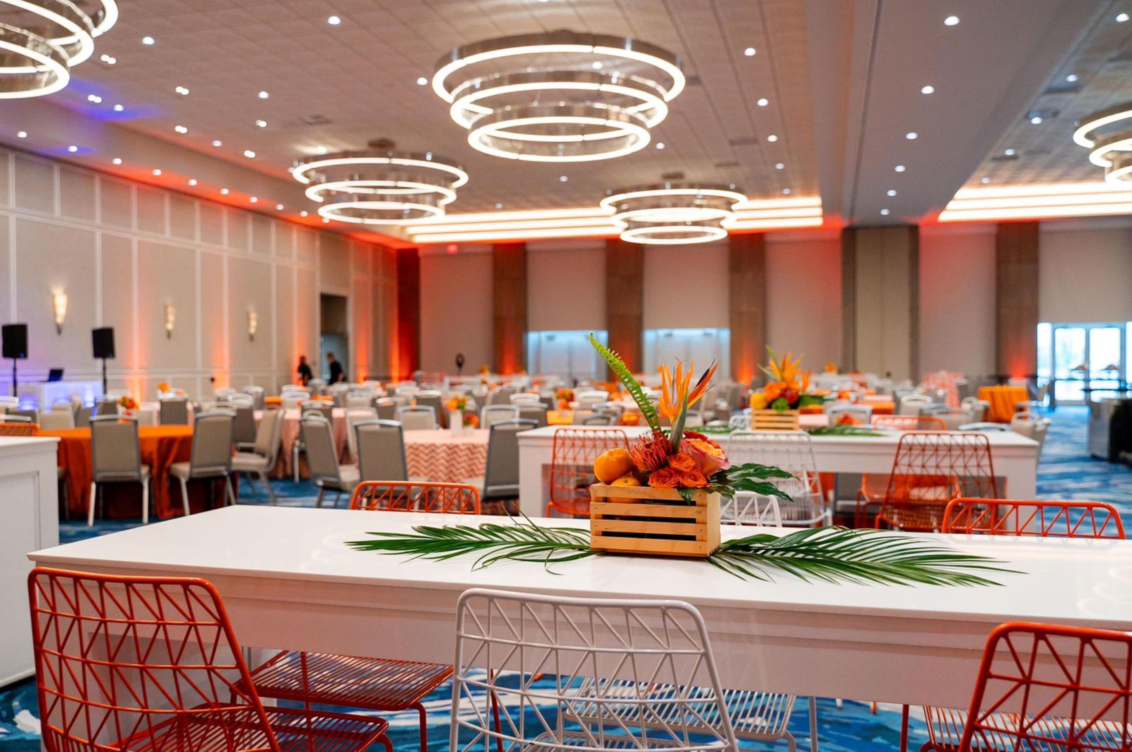 A spacious banquet hall with multiple tables, modern lighting fixtures, and a central floral arrangement.