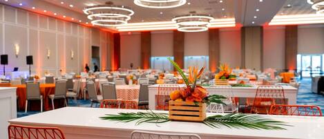 A spacious banquet hall with multiple tables, modern lighting fixtures, and a central floral arrangement.