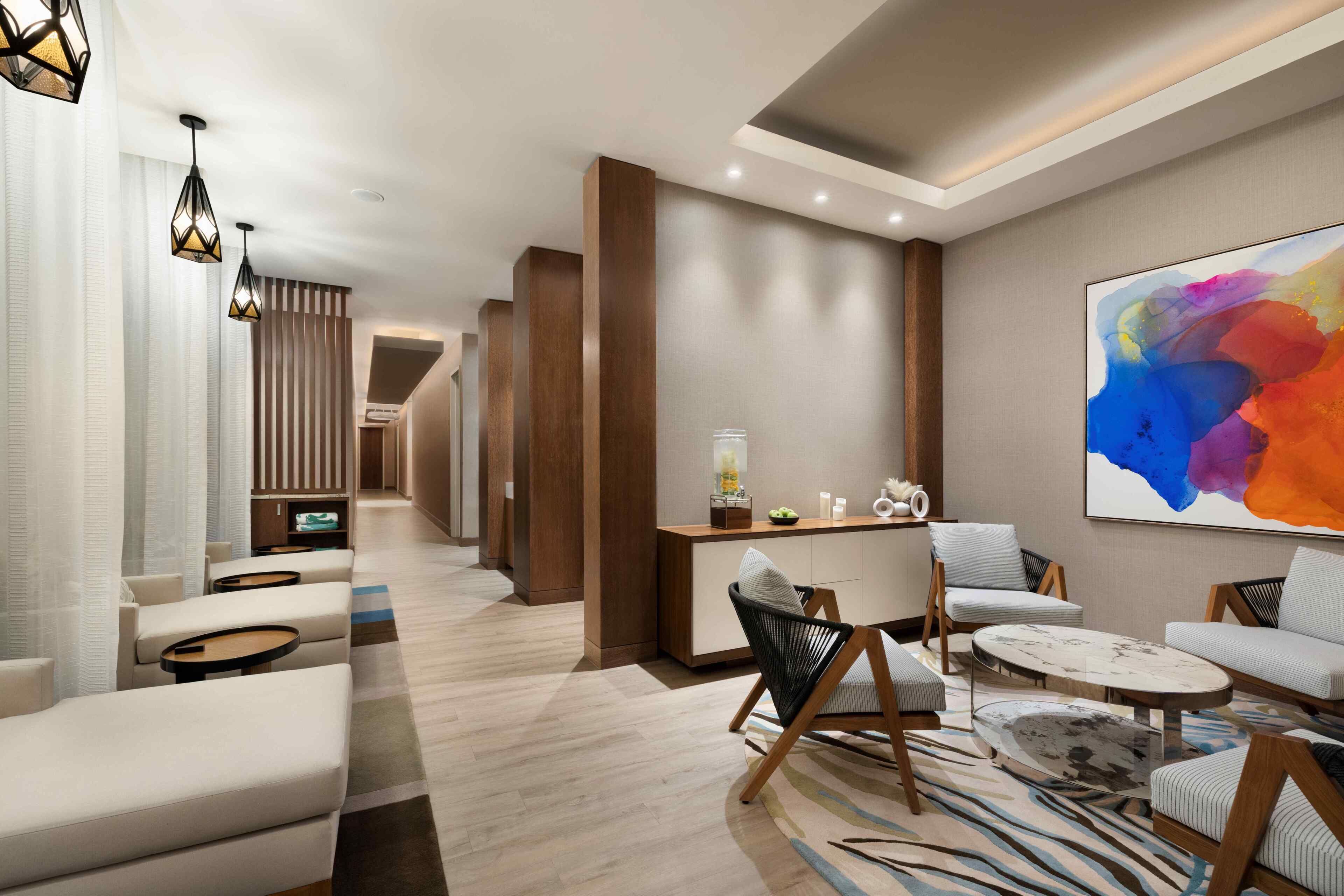 A modern hotel lobby with a seating area, a reception desk, and a colorful abstract painting.