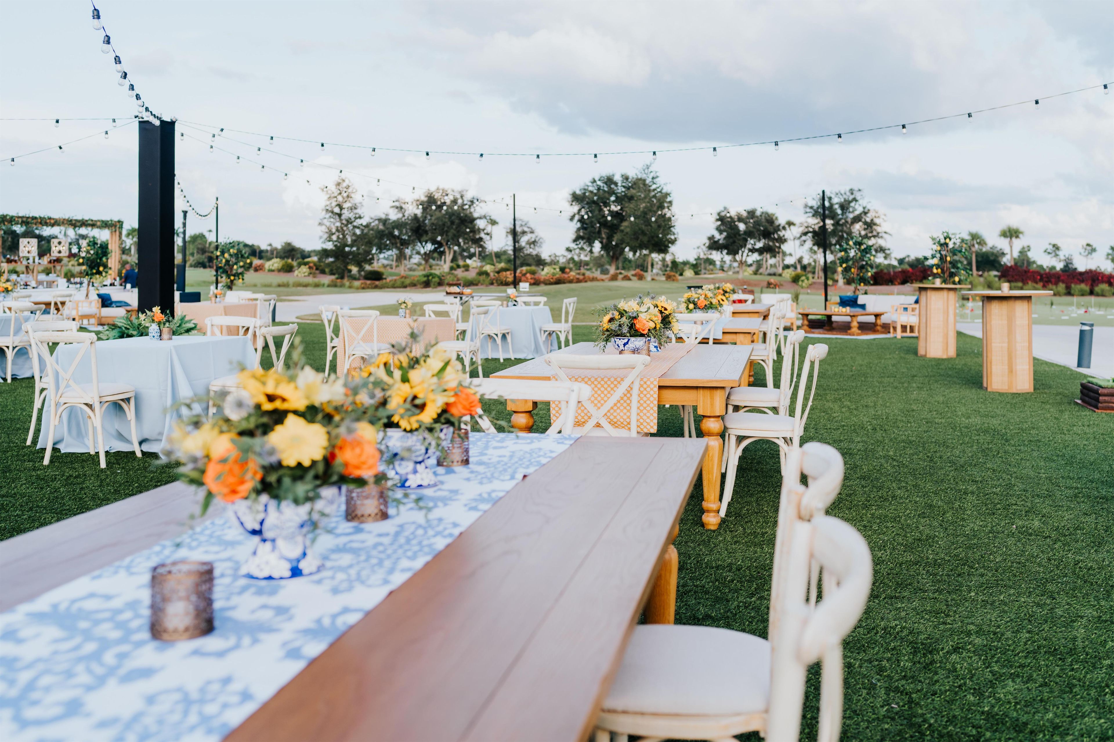 An outdoor event space with tables set for guests, surrounded by greenery and string lights.