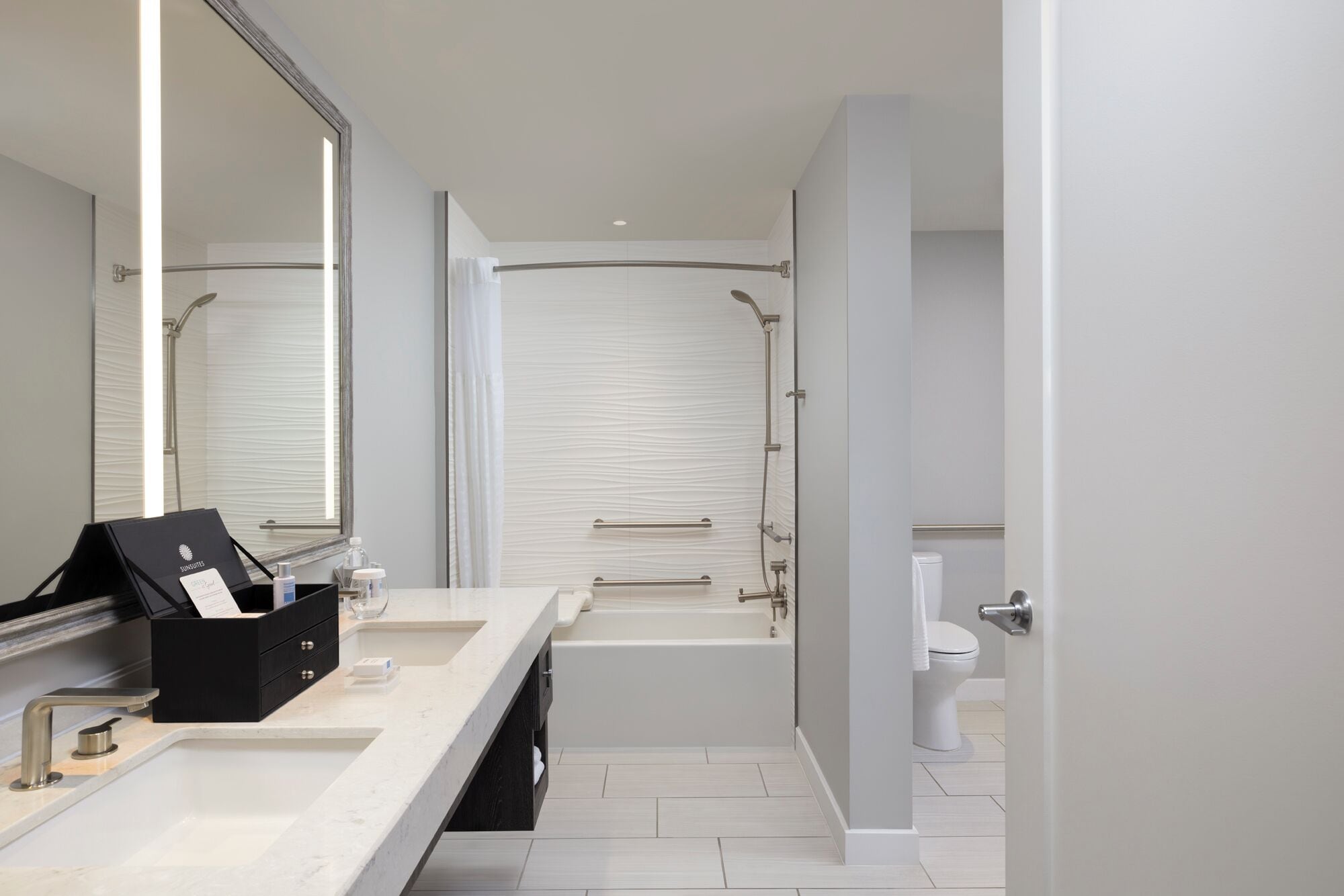 Een moderne badkamer met een grote spiegel, een badkuip, een toilet en een wastafelmeubel met wastafel.
