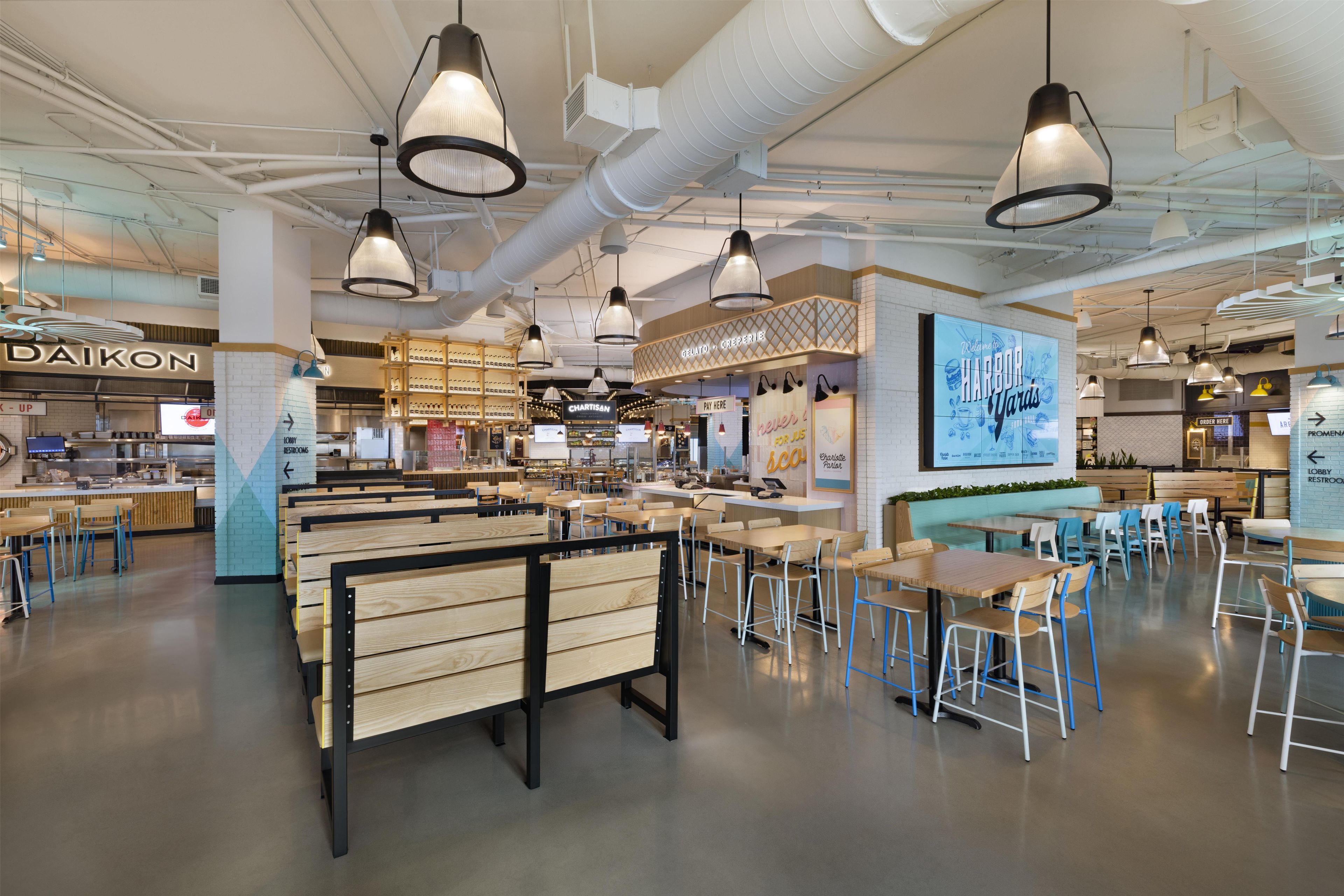 Ein modernes Café-Interieur mit verschiedenen Sitzbereichen, darunter Boxsitzgelegenheiten und Tische, sowie einer gut sichtbaren Theke mit Speisekarte.