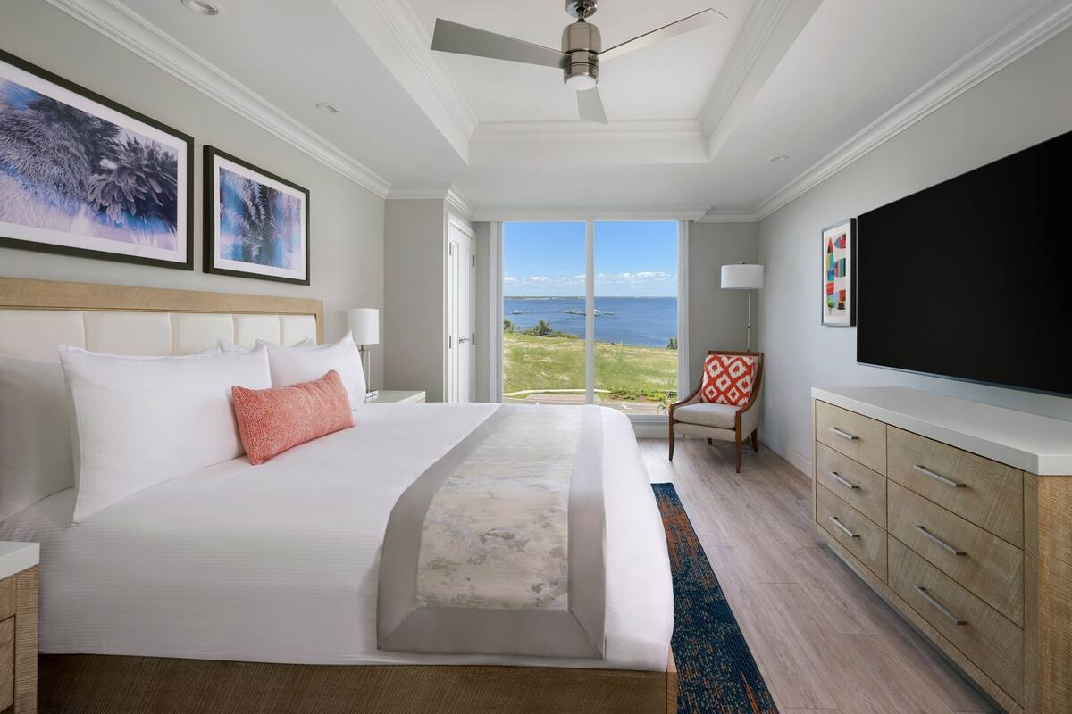 Habitación de hotel con una cama grande, televisión de pantalla plana, ventilador de techo y vista al océano.