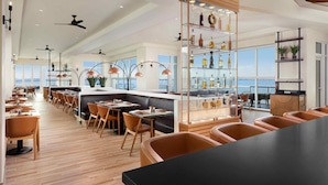 A modern restaurant with high ceilings, multiple ceiling fans, and a bar area with a glass display case. - Sunsuites Villas At Sunseeker Resort, Curio By Hilton (Charlotte Harbor)