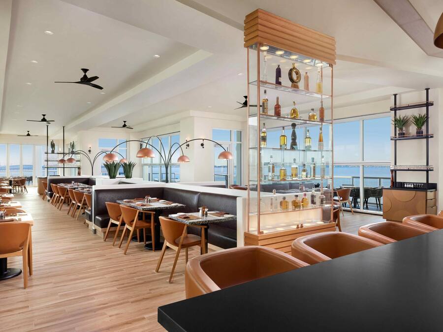 A modern restaurant with high ceilings, multiple ceiling fans, and a bar area with a glass display case.