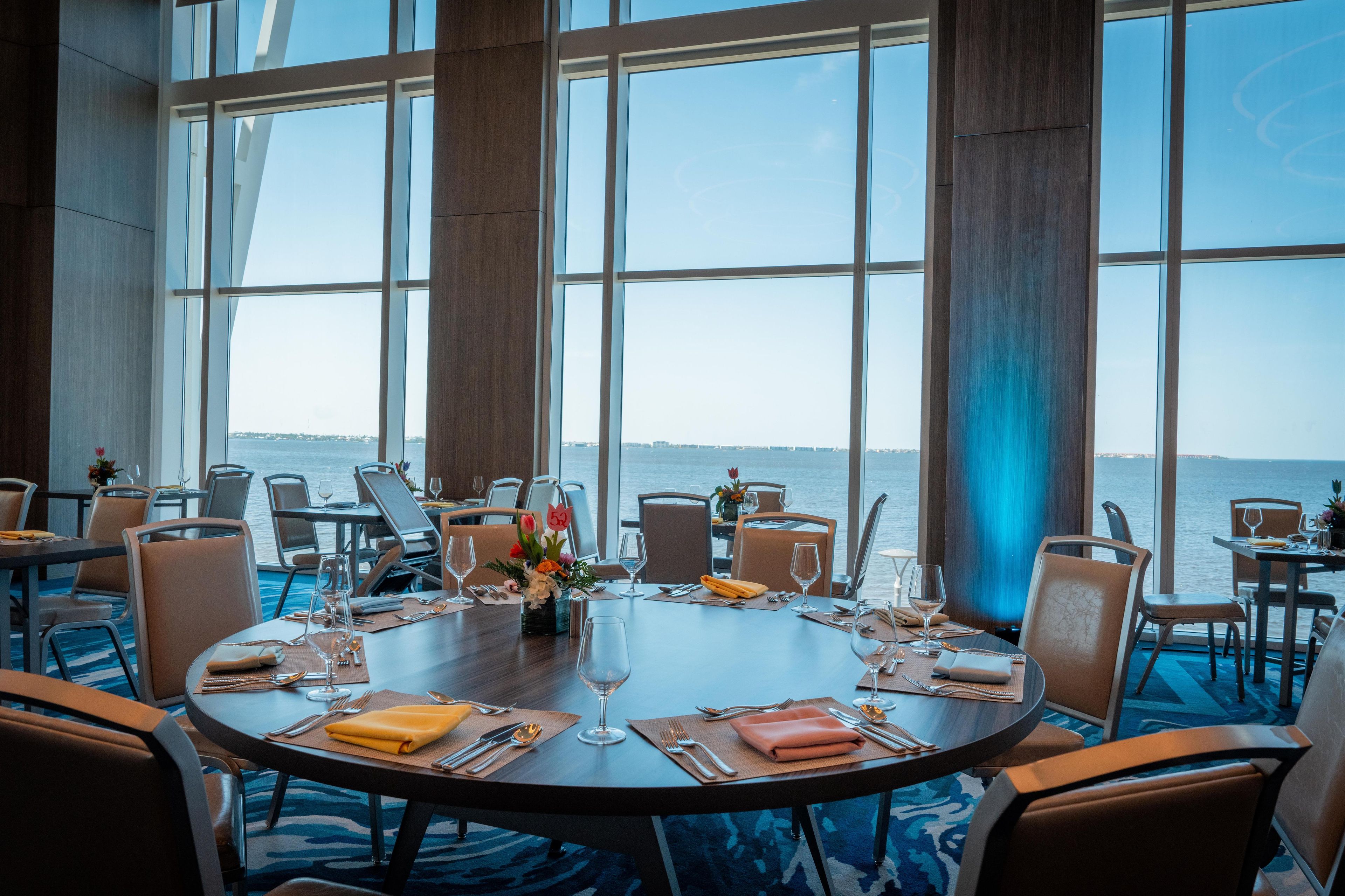 Un comedor con mesas redondas, sillas y vista al mar.