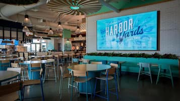 A spacious indoor dining area with multiple tables and chairs, a large illuminated welcome sign, and a brick wall.
