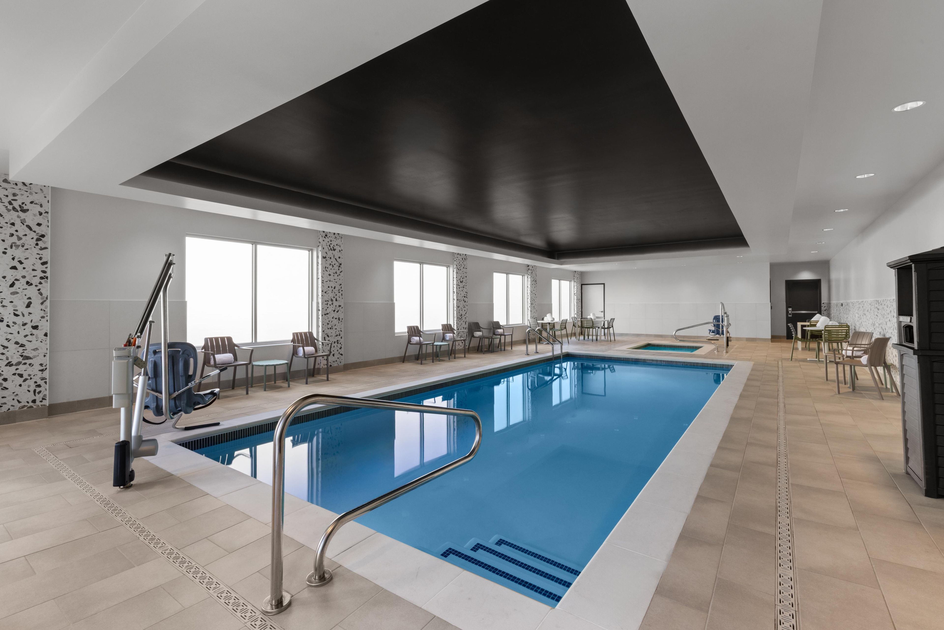 Una gran piscina interior con diseño moderno, rodeada de zonas de estar y un techo alto.