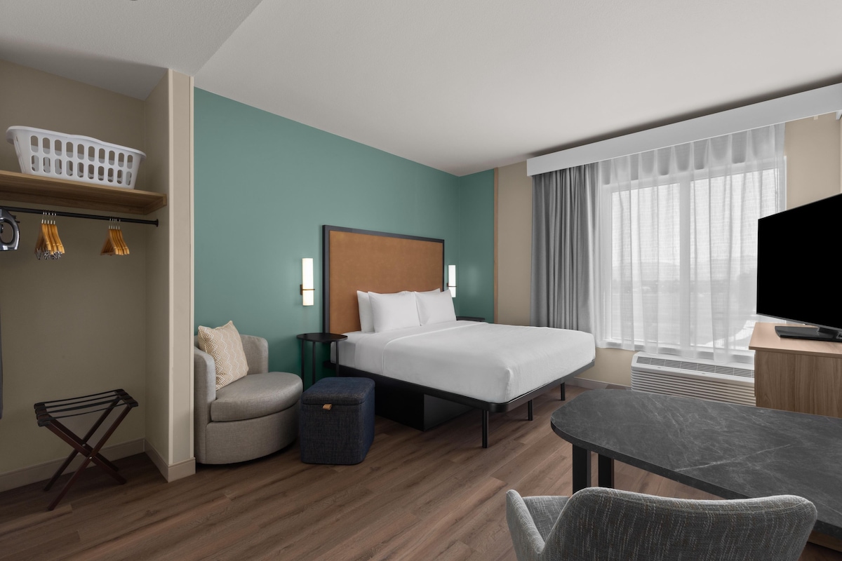 Une chambre d’hôtel équipée d’un lit, d’un bureau, d’une chaise, d’une télévision et d’une fenêtre avec des rideaux.