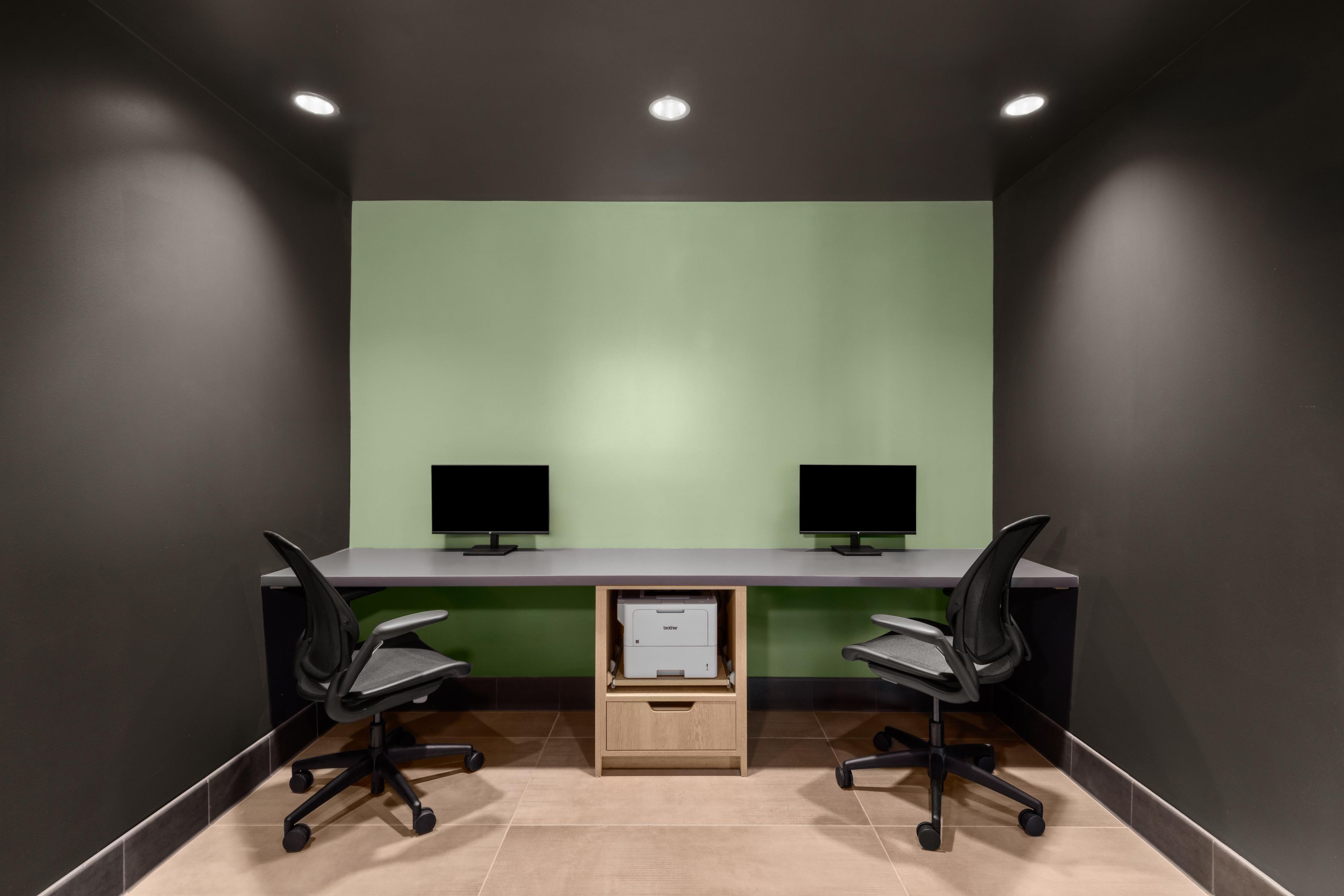 A conference room with two desks, each with a monitor, chairs, and a printer.