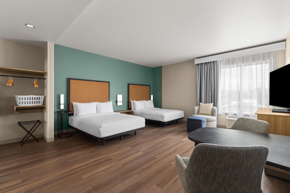 Une chambre d’hôtel avec deux lits, un bureau, une chaise, une télévision et une fenêtre avec des rideaux.