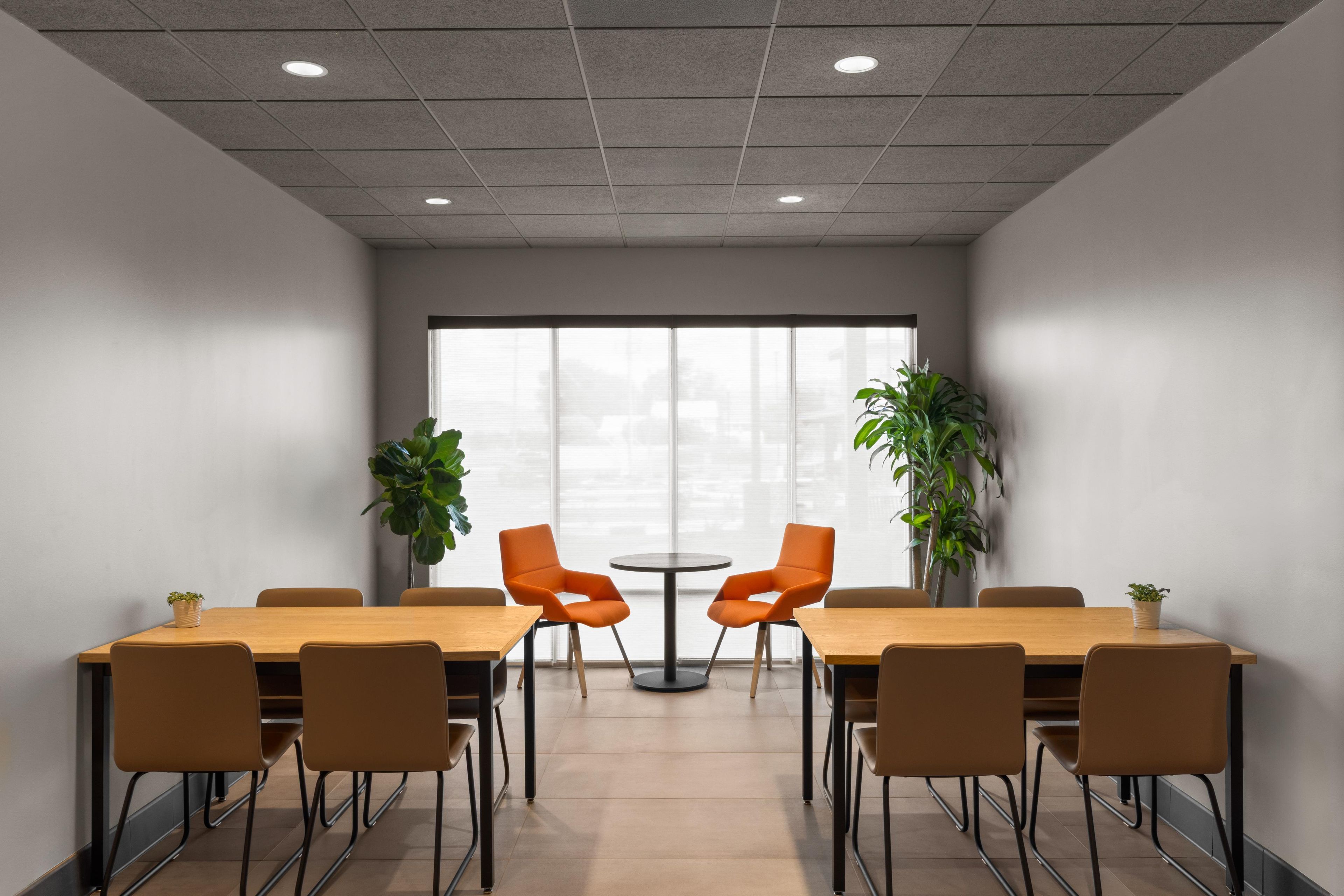 Een congreszaal met een lange tafel, meerdere stoelen, een kleine ronde tafel en twee potplanten.