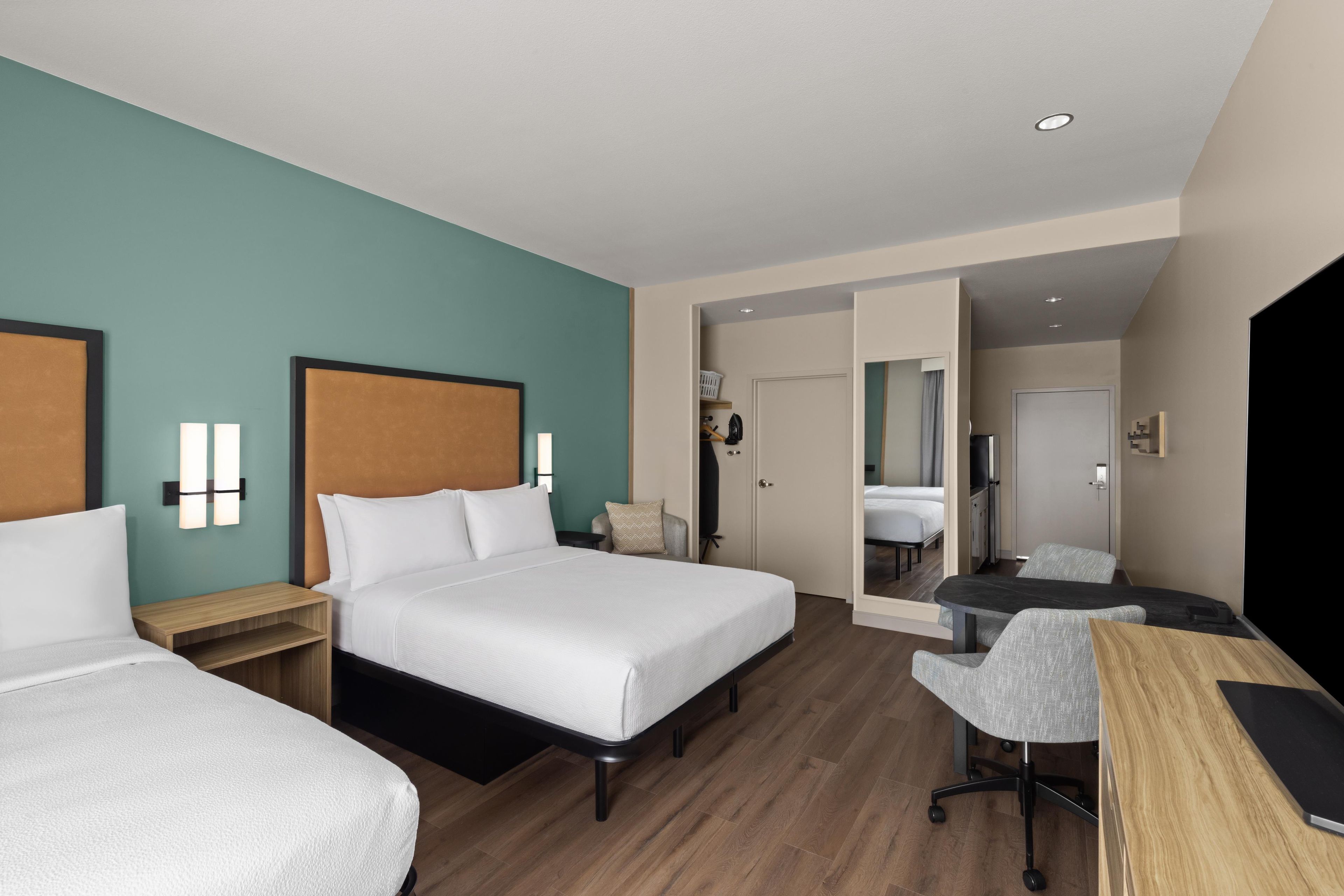 A hotel room with two beds, a desk, a chair, and a bathroom visible through an open door.