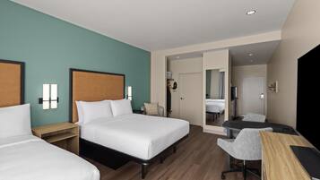 Habitación de hotel con dos camas, un escritorio, una silla y un baño visible a través de una puerta abierta.