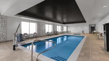 A large indoor swimming pool with a modern design, surrounded by seating areas and a high ceiling.