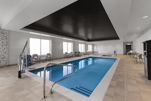 Una gran piscina interior con diseño moderno, rodeada de zonas de estar y un techo alto.