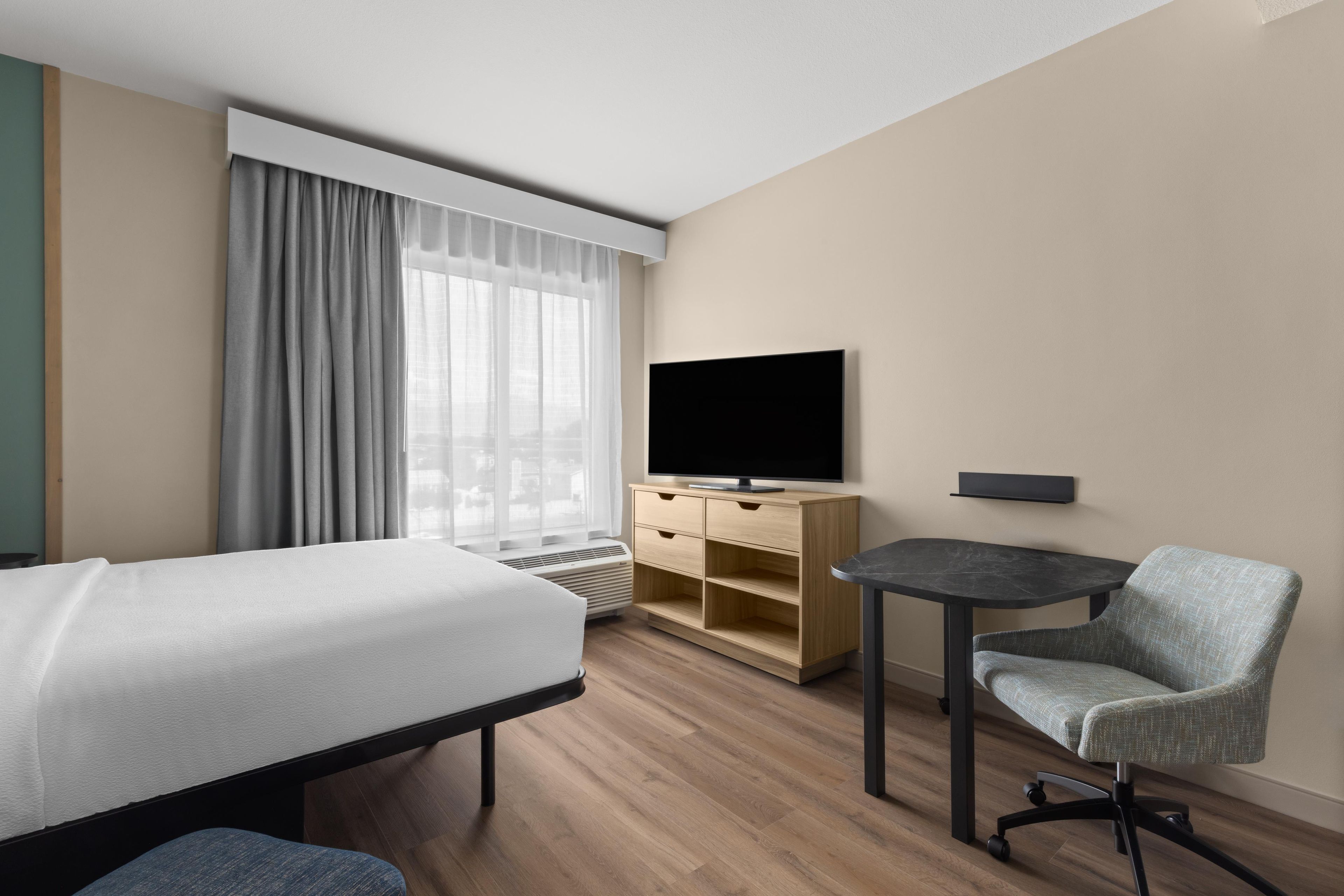 Habitación de hotel con cama, escritorio, silla, televisión y ventana con cortinas.