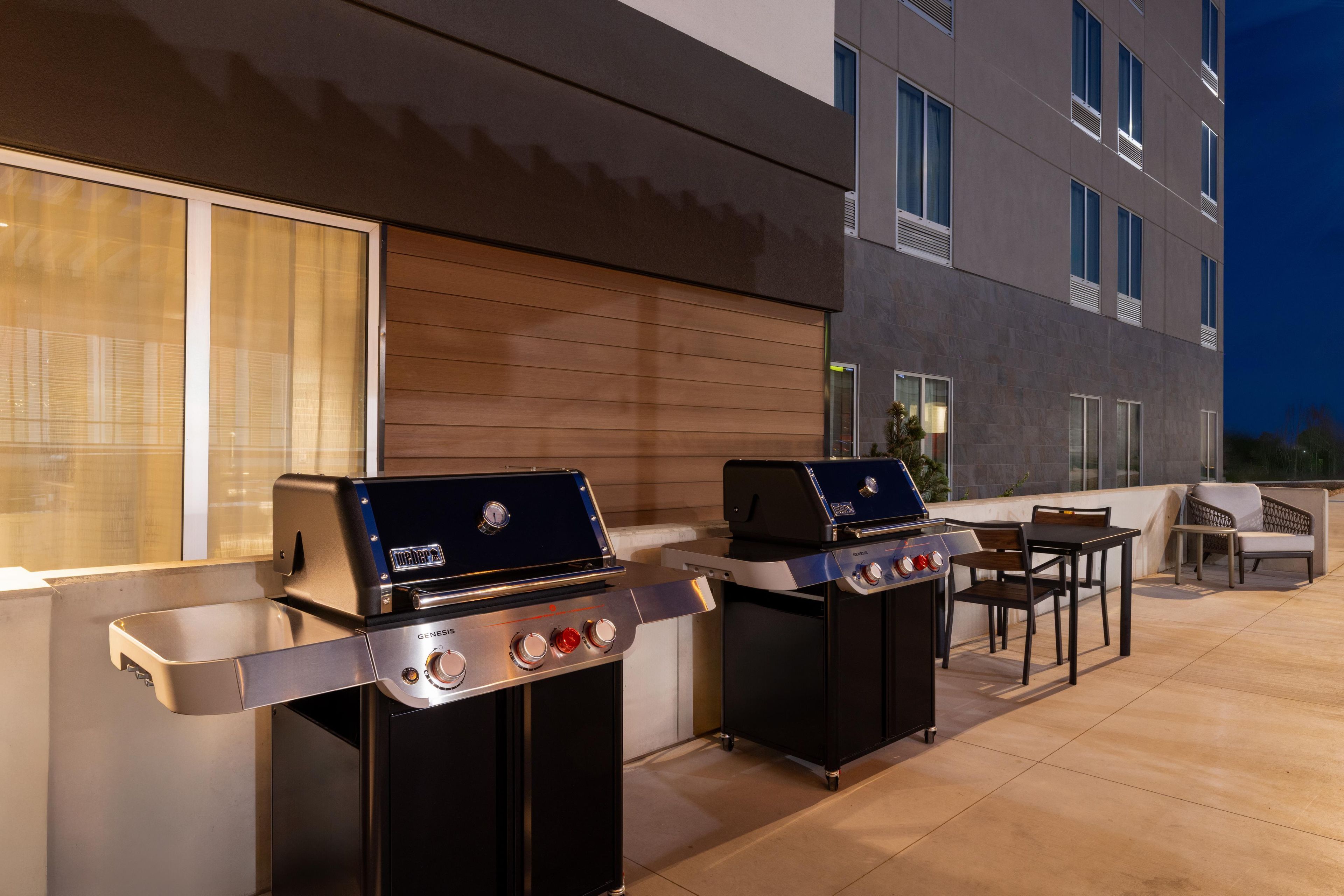 An outdoor patio with two barbecue grills, a table, and chairs.