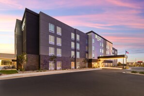 A modern hotel building with a flat roof, multiple windows, and a well-lit entrance. - LivSmart Studios by Hilton Salt Lake City West Valley City (West Valley City)