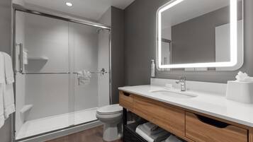 A modern bathroom with a glass-enclosed shower, a toilet, a vanity with a mirror, and a towel rack.