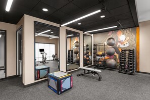 A gym with exercise equipment, mirrors, and a wall with a colorful mural.