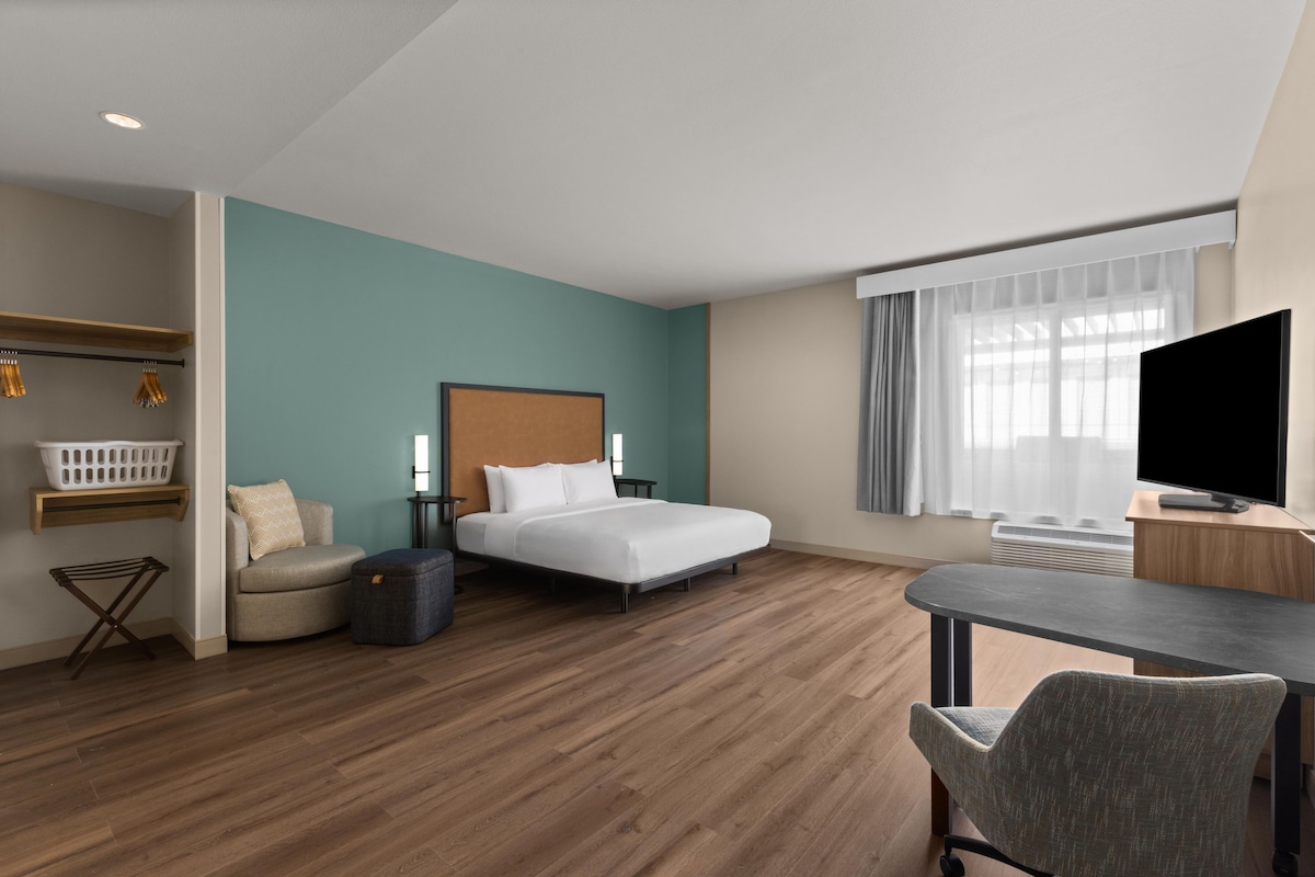 Une chambre d’hôtel comprenant un lit, un bureau avec une télévision, une chaise, une petite table, un panier à linge et un étendoir.
