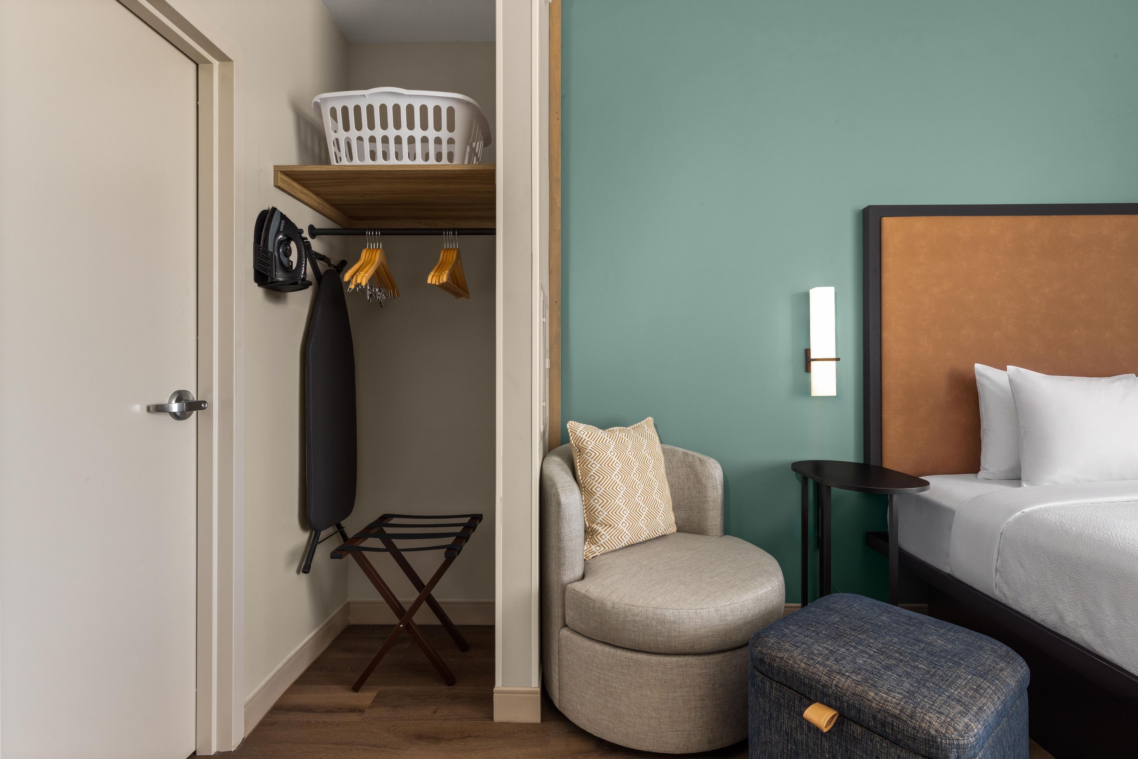 A hotel room with a bed, a chair, a small table, a laundry rack, and a closet.