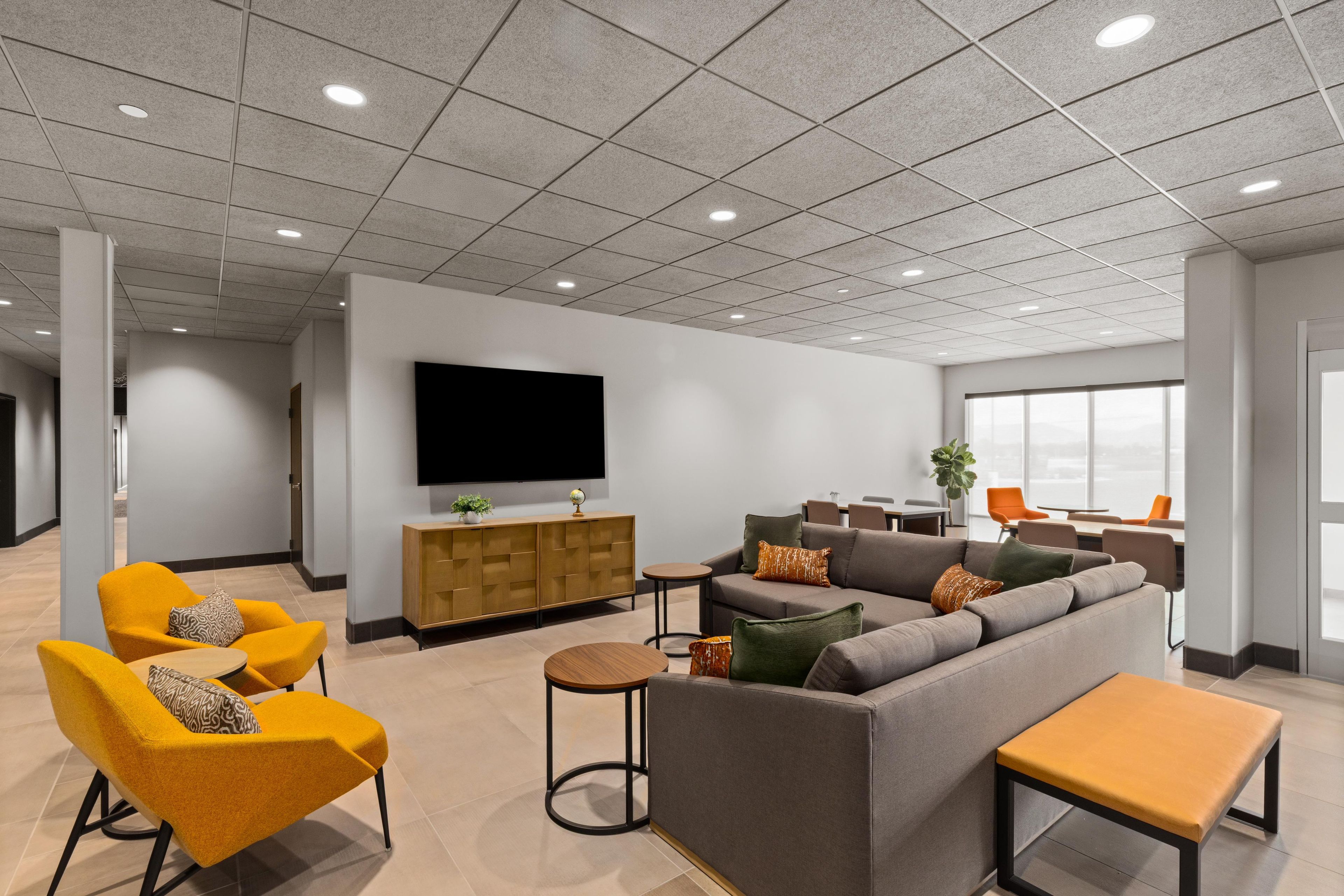 A modern interior with a grey sofa, yellow chairs, a wooden cabinet, and a television on the wall.
