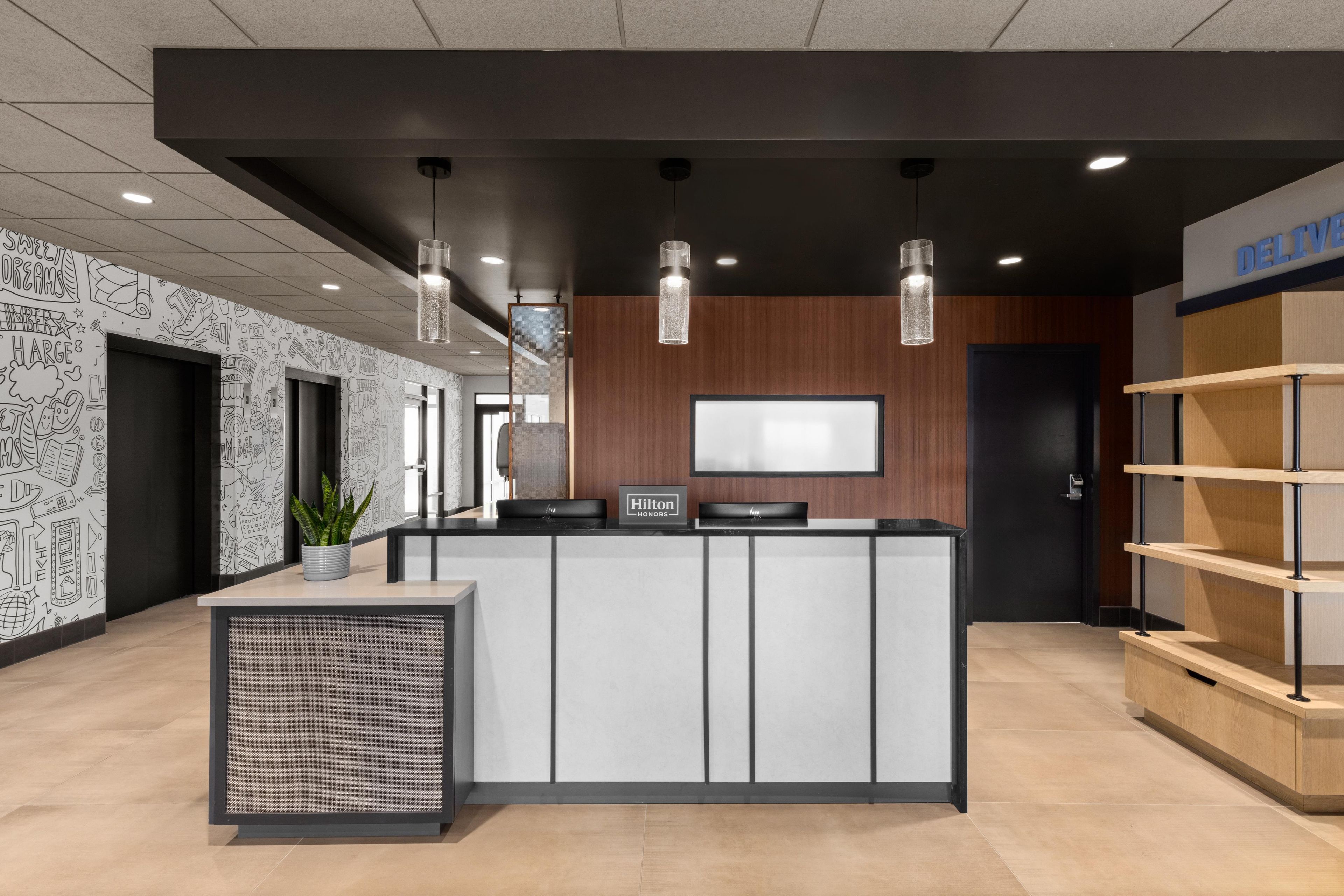 A modern reception desk with a flat-screen TV, a potted plant, and a sign reading 'Hilton Honors'.