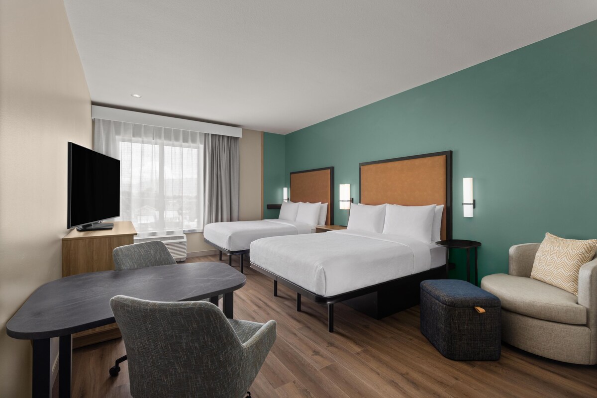 Une chambre d’hôtel avec deux lits, un bureau, une chaise, une télévision et une vue sur la ville.