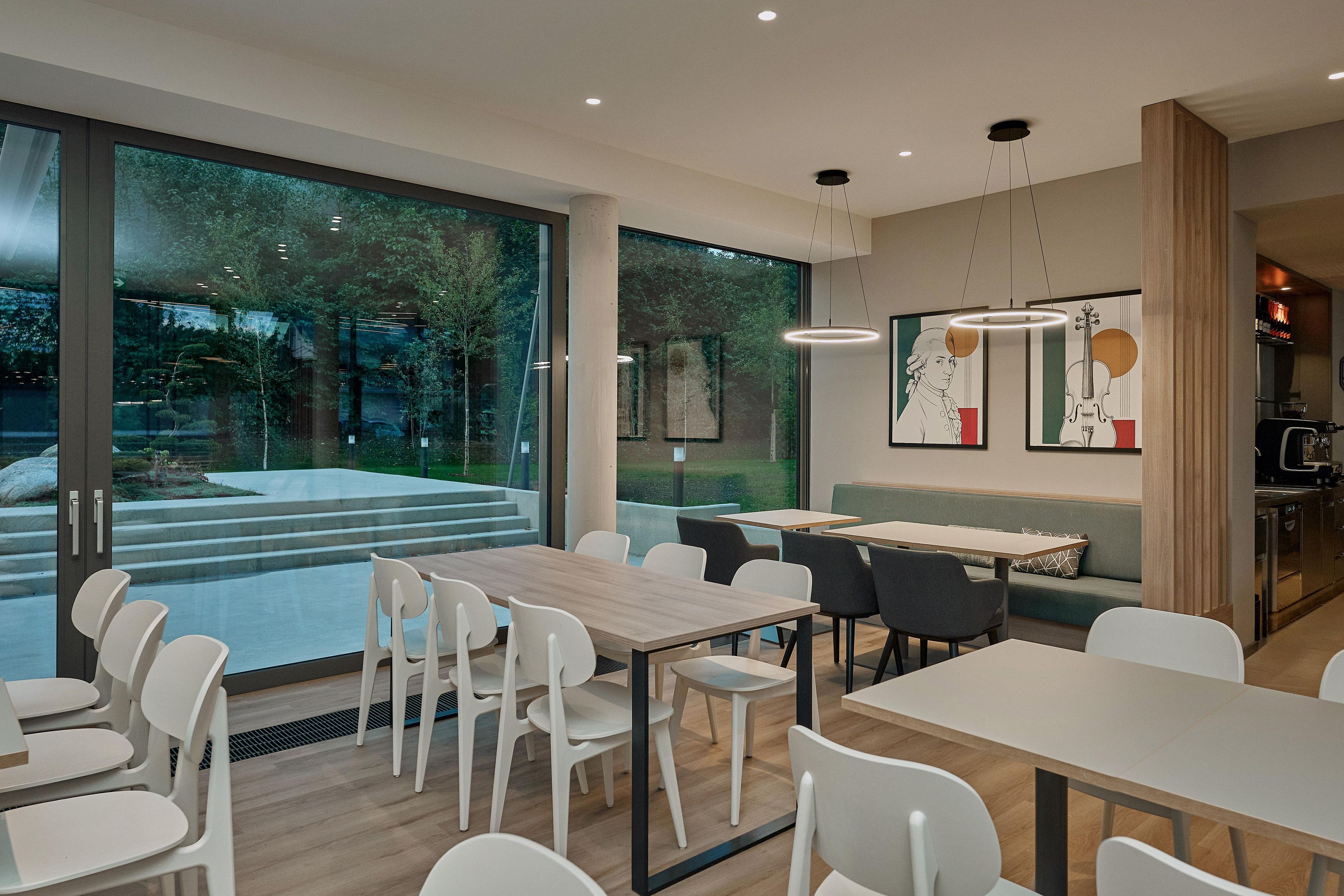 Un espace repas moderne, avec des tables et des chaises, de grandes fenêtres et des œuvres d’art accrochées aux murs.