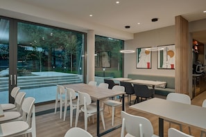 Een moderne eetruimte met tafels en stoelen, grote ramen en kunstwerken aan de muren.
