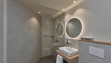 Un baño moderno con ducha envuelta en vidrio, un lavamanos con tocador de madera y dos espejos montados en la pared.