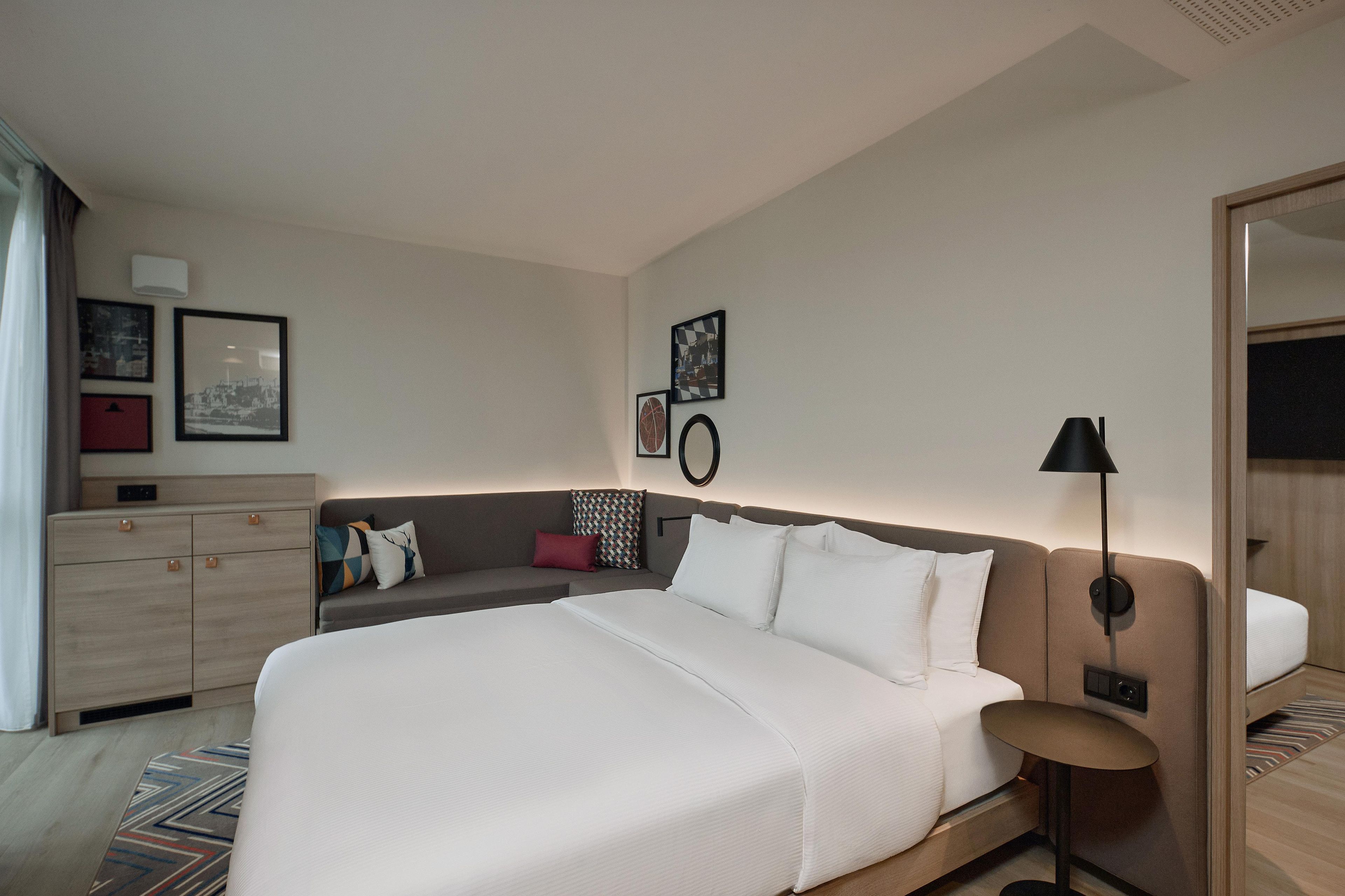 Una habitación de hotel moderna con una cama grande, un sofá, un escritorio y una lámpara.