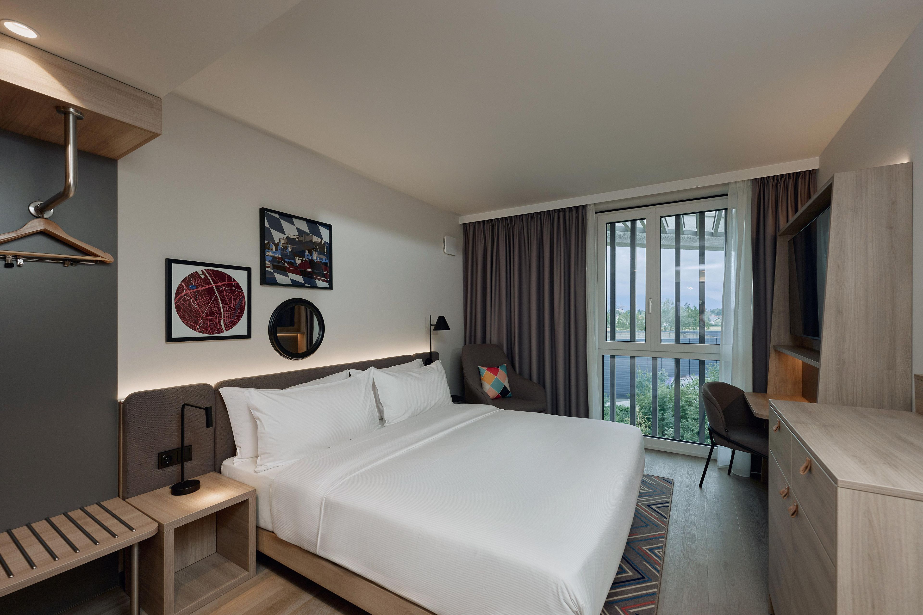 Ein Hotelzimmer mit Bett, Nachttisch, Schreibtisch, Stuhl und einem großen Fenster mit Vorhängen.