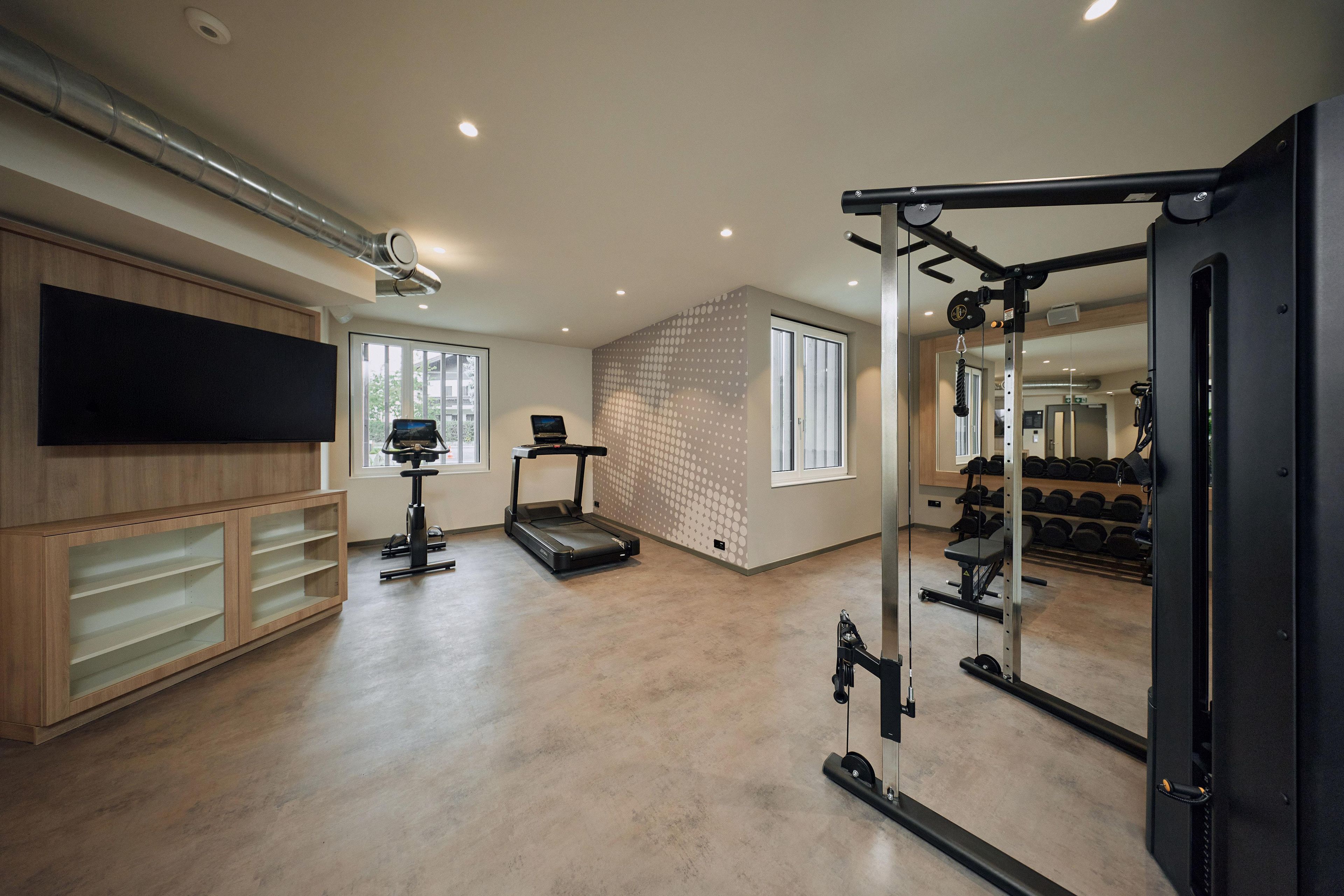 Una palestra in casa con tapis roulant, pesi e televisore.