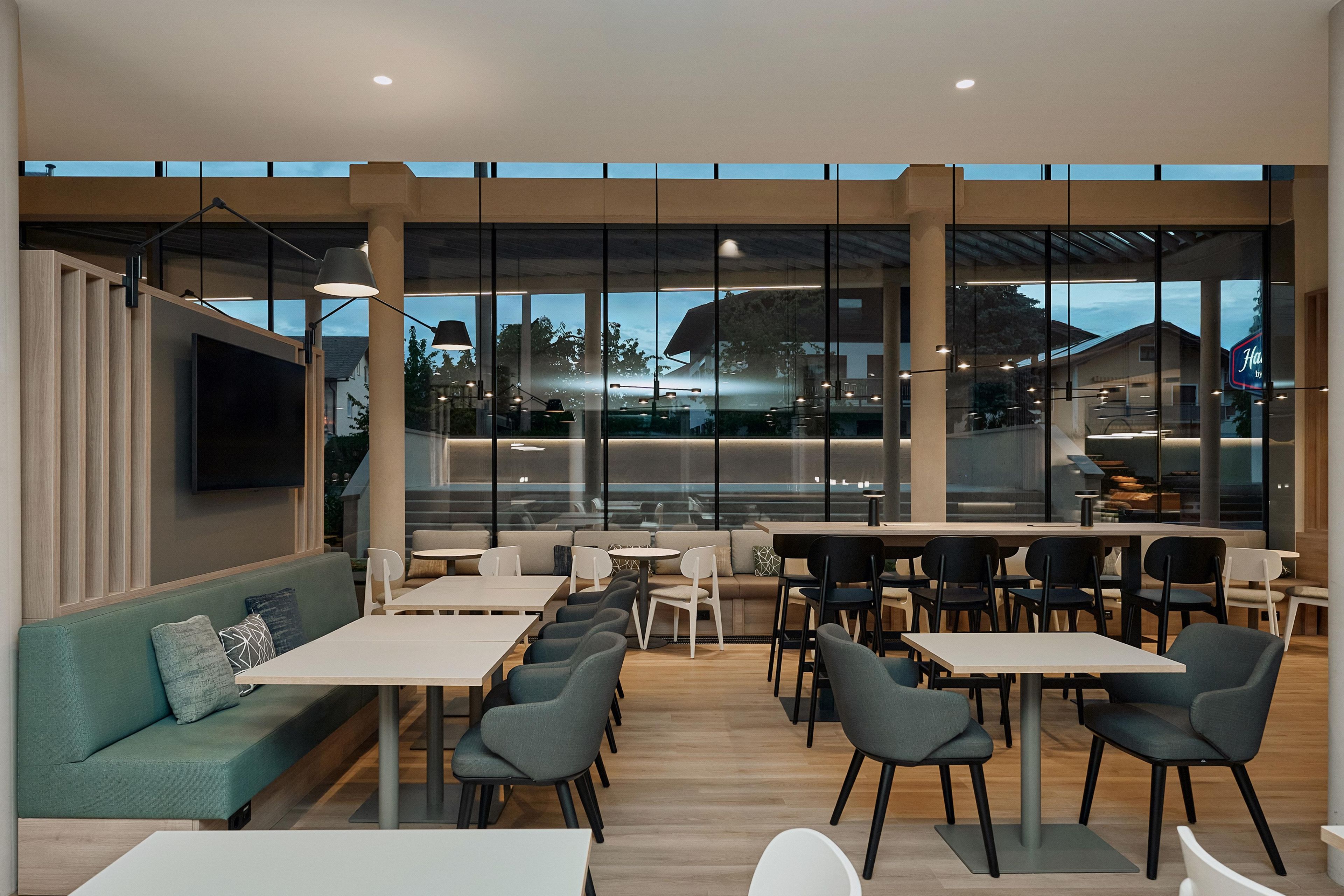 A modern interior with a seating area, tables, and a large window offering a view of the outside.