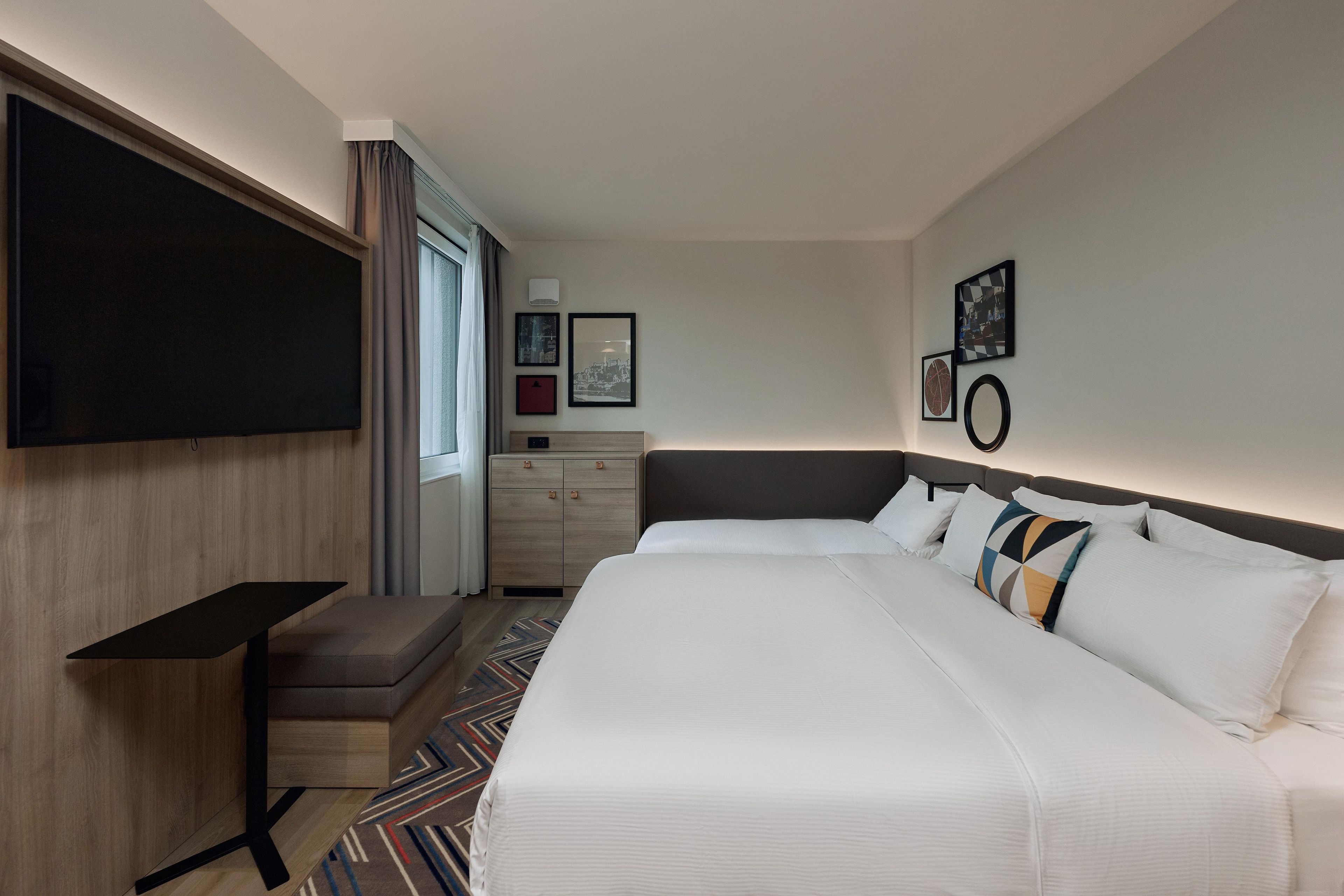 Ein Hotelzimmer mit einem großen Bett, einem Flachbildfernseher, einem Schreibtisch und einer Kommode.