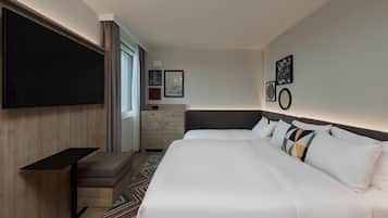 Ein Hotelzimmer mit einem großen Bett, einem Flachbildfernseher, einem Schreibtisch und einer Kommode.