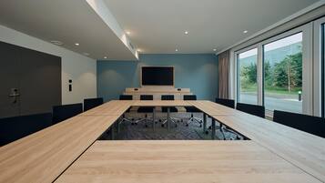 A conference room with a long table, chairs, a large screen, and a view through the windows.