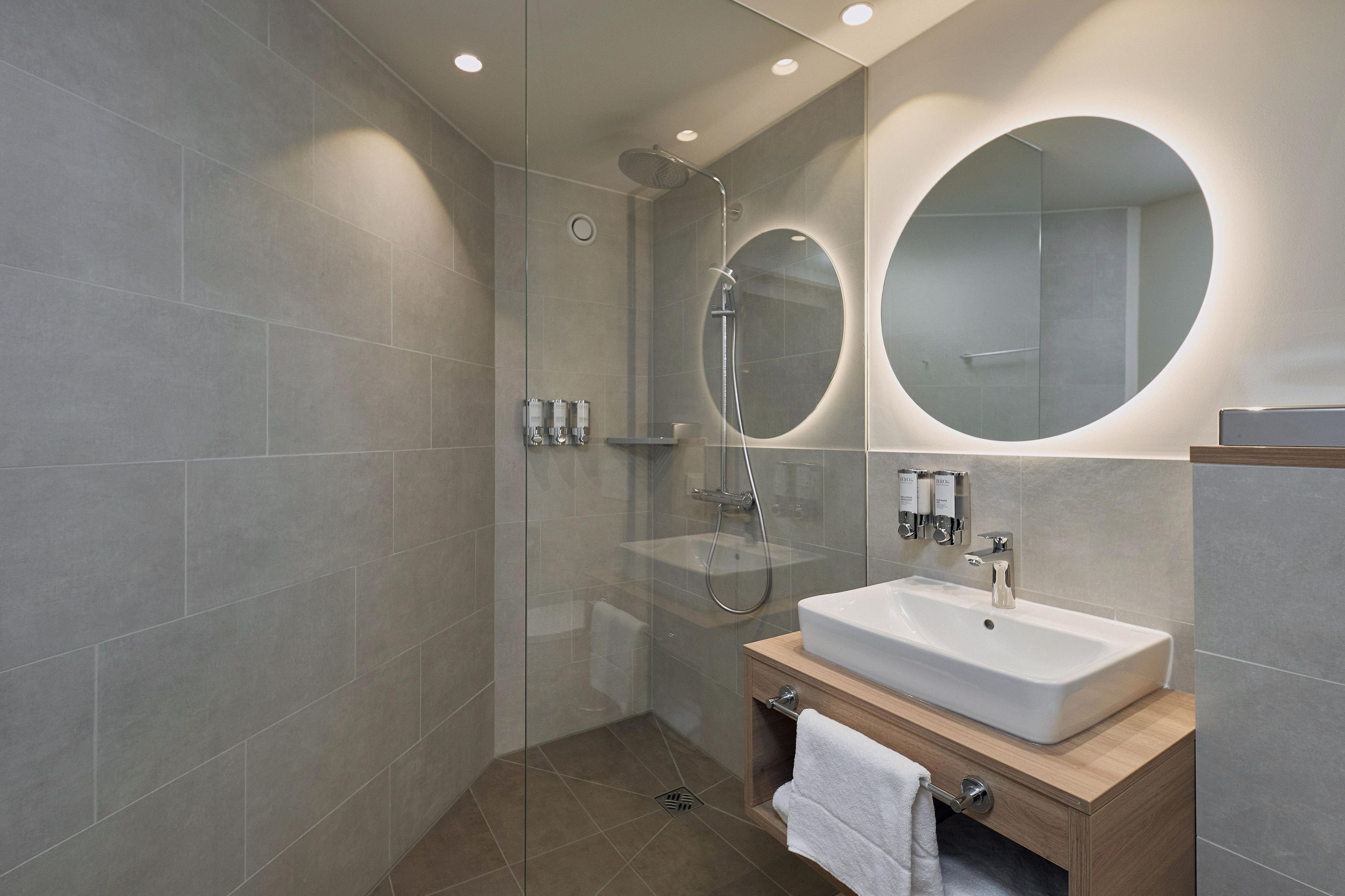Un baño moderno con ducha acristalada, lavabo con tocador de madera y un espejo grande.