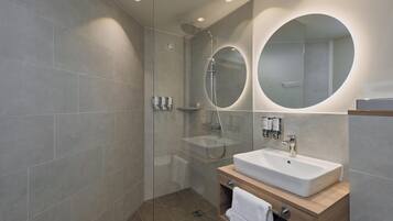 Un baño moderno con ducha acristalada, lavabo con tocador de madera y un espejo grande.