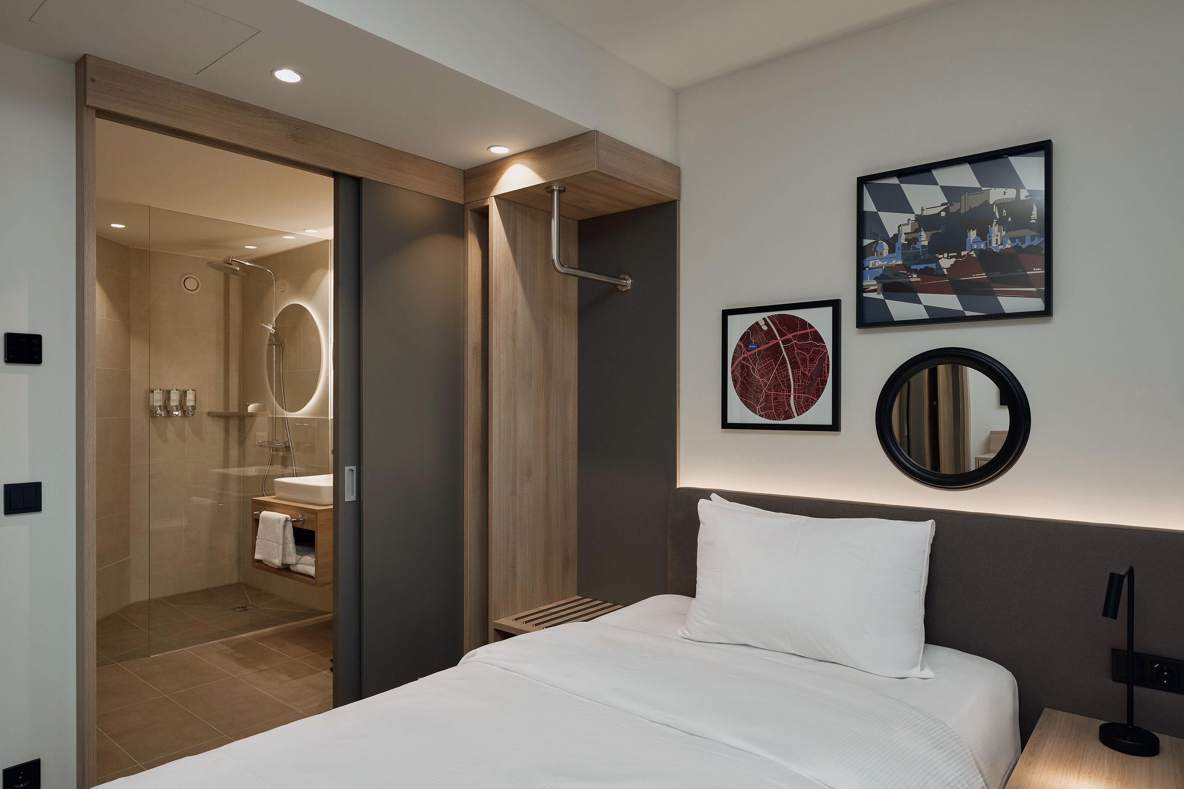 Ein Hotelzimmer mit einem Bett, einer Dusche, einem Waschbecken und zwei gerahmten Bildern an der Wand.