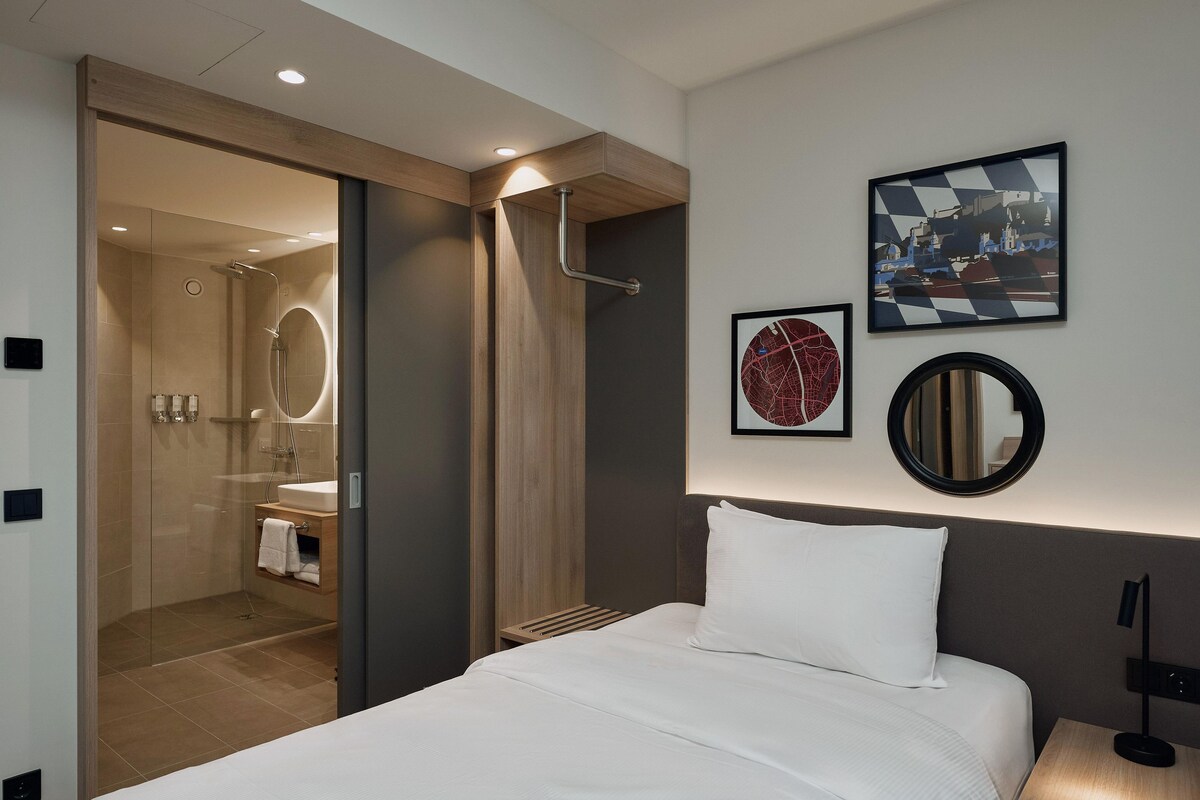 Ein Hotelzimmer mit einem Bett, einer Dusche, einem Waschbecken und zwei gerahmten Bildern an der Wand.