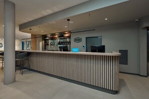 Un espace bar moderne avec un comptoir en bois, un écran numérique et un assortiment de bouteilles.