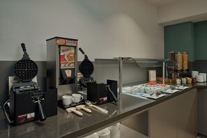 Un buffet de petit-déjeuner en libre-service avec des appareils à gaufres, des machines à café et un choix varié d’aliments.